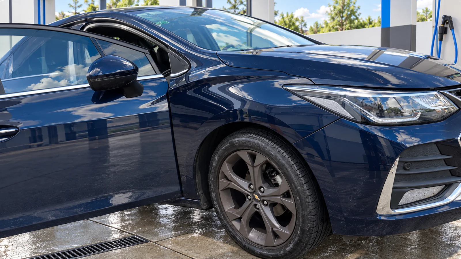 Chevrolet Cruze II azul oscuro, detalle delantero y puerta abierta, en un lavadero con ambientación recreada.